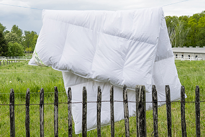 Die Winter-Bettdecke mit Gänsedaunen und Gänsefedern hängt an der frischen Luft an einer Wäscheleine zum auslüften
