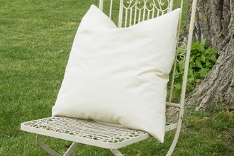 Eine Kissenfüllung ist auf einen alten weißen Gartenstuhl aus Metall platziert, er steht vor einer großen Pappel von der man nur den Baumstamm sieht