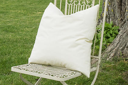 Eine Kissenfüllung ist auf einen alten weißen Gartenstuhl aus Metall platziert, er steht vor einer großen Pappel von der man nur den Baumstamm sieht
