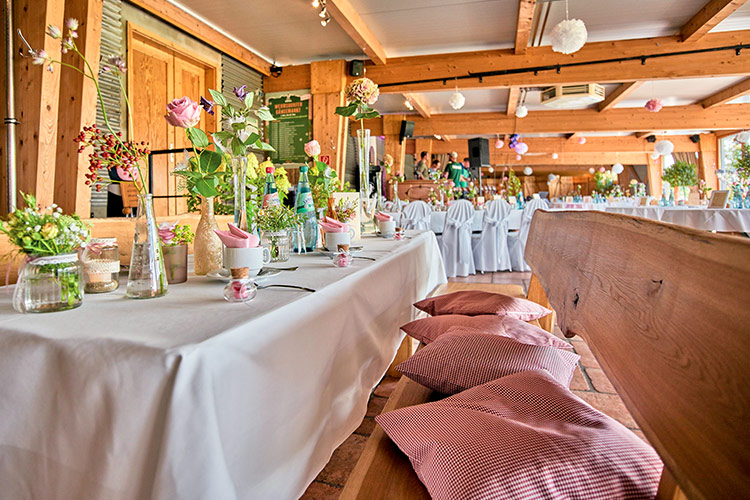 Großer Saal mit rustikalen Holzbalken und weißen Hessen über den Stühlen, Blumendekoration für eine Hochzeit