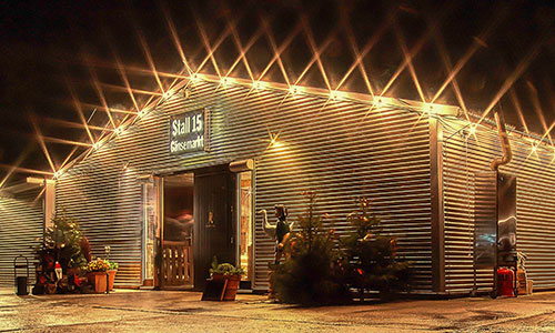 Herzlich willkommen! Der weihnachtliche Gänsemarkt ist für Sie geöffnet vom 1. November bis 22. Dezember, täglich von 10 bis 19 Uhr, warme Küche von 10:30 bis 18:30. Wir wünschen unseren Gästen eine schöne Vorweihnachtszeit. Stall 15 auf dem Gänsemarkt Wermsdorf am Abend, wunderschön beleuchtet mit Lichterketten am Dachfirst, das Tor ist einladend geöffnet